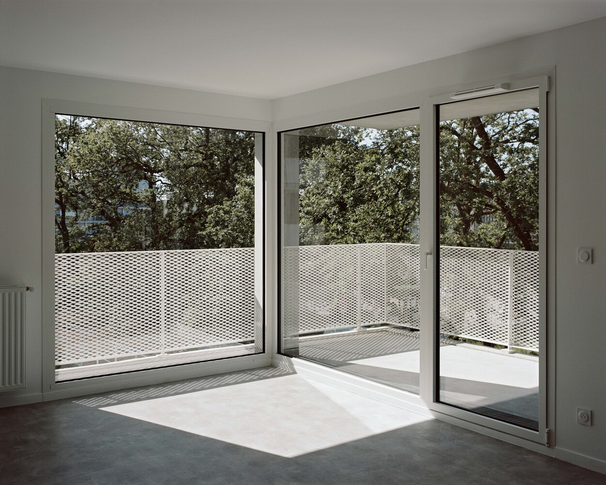 Corner room with glass doors opening to a balcony with perforated metal railing in morning light
