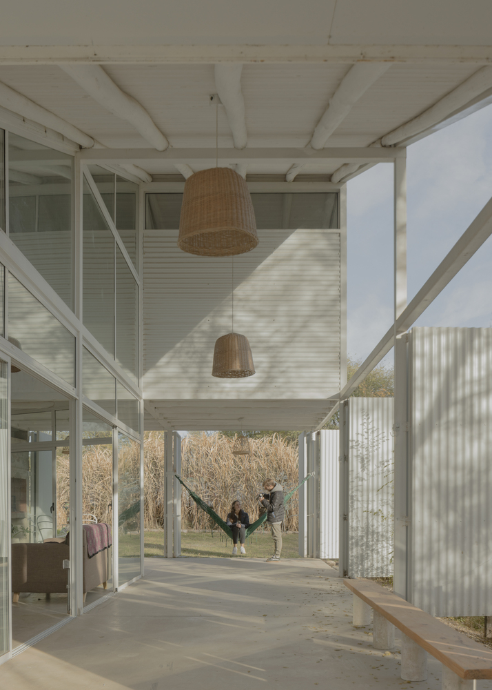 Covered porch with white timber beams and wicker pendant lamps overlooking a grassy yard with bare trees