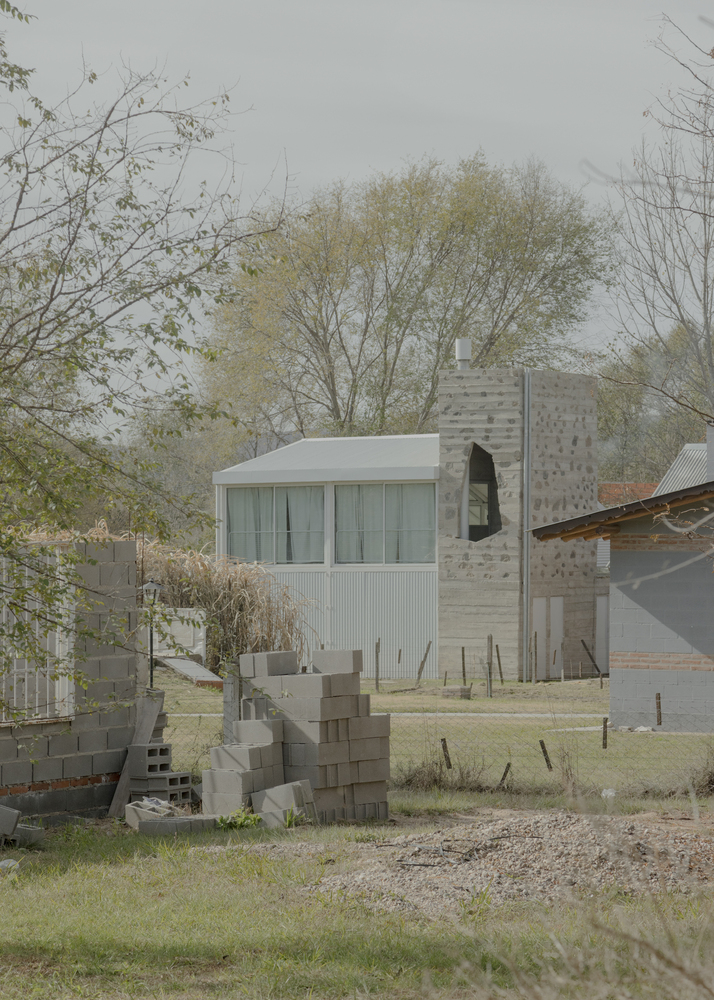 White corrugated metal volume beside a board-formed concrete tower among bare spring trees