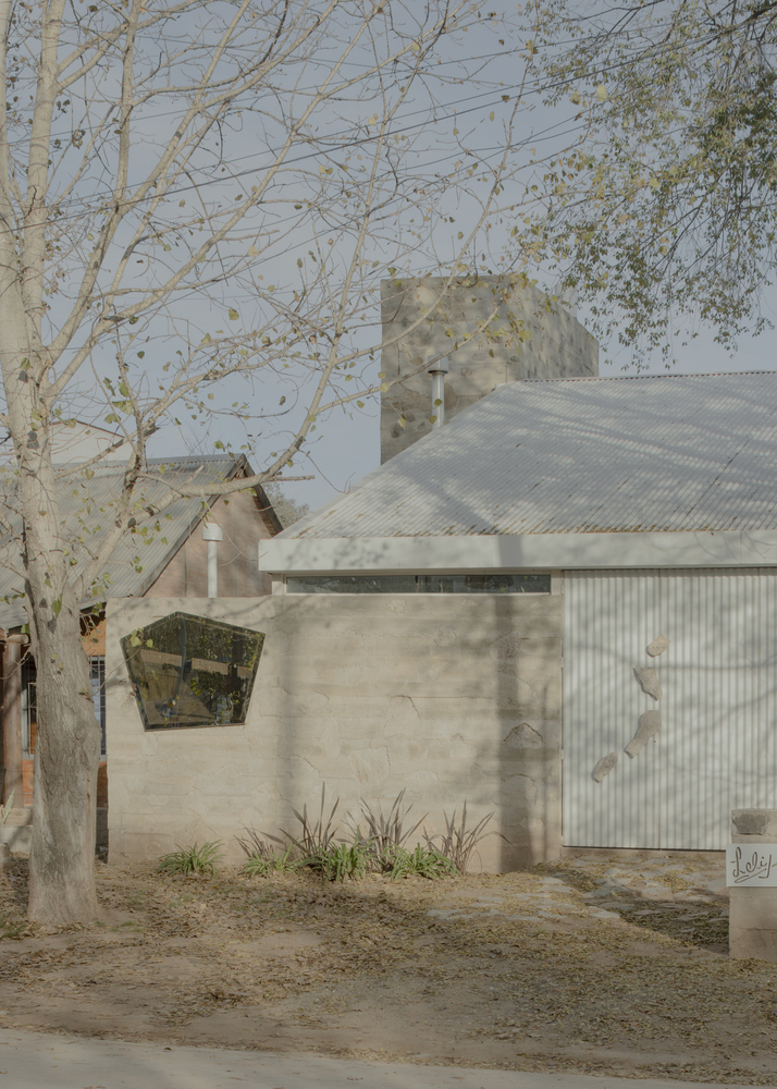 Street view of board-formed concrete walls and corrugated metal roof beneath dappled tree shadows