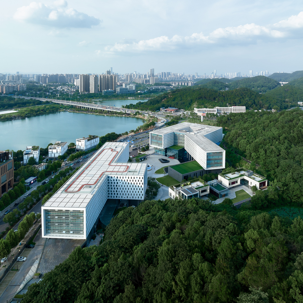 Aerial view of the campus complex with white perforated facades nestled among forested hills and a lake