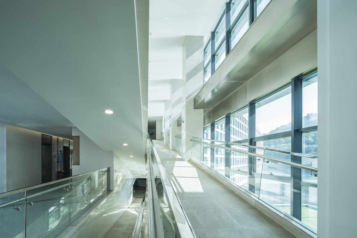 Interior corridor with glass balustrade and full-height windows overlooking the courtyard in bright daylight