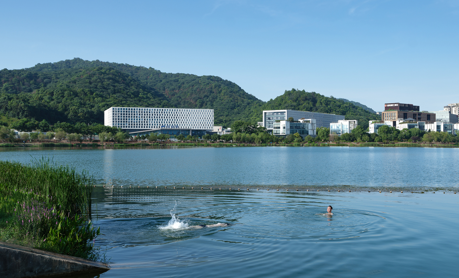 View across the lake with swimmers in the foreground and the perforated white volume against forested hills