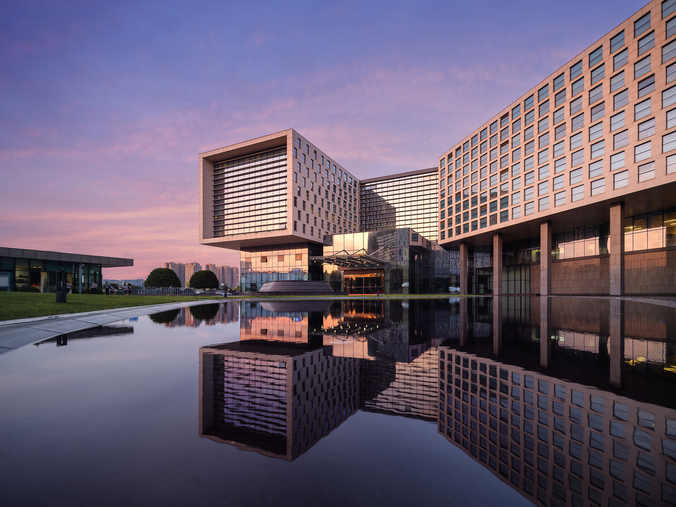 Reflecting pool mirroring the cantilevered volumes and patterned facades at dusk with pink sky