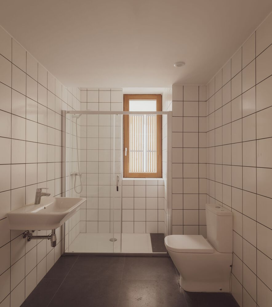 White tiled bathroom with glass shower partition and timber-framed window with vertical slat screen