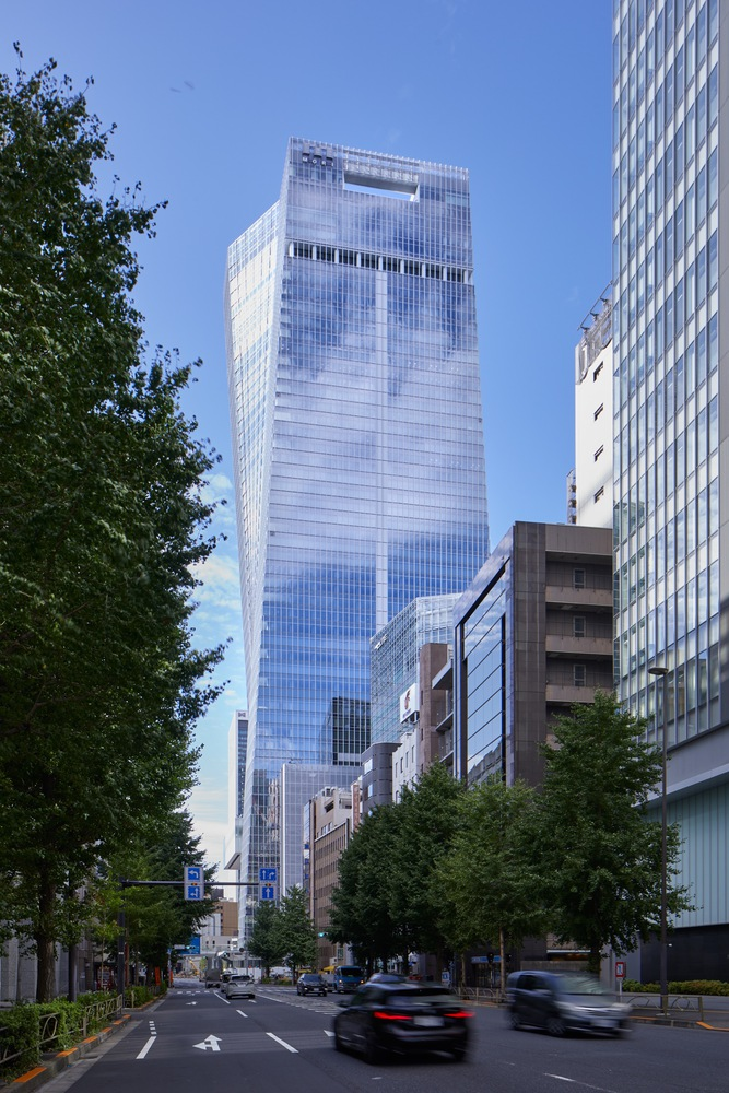 Street view of the glass tower rising above tree-lined boulevard with passing traffic