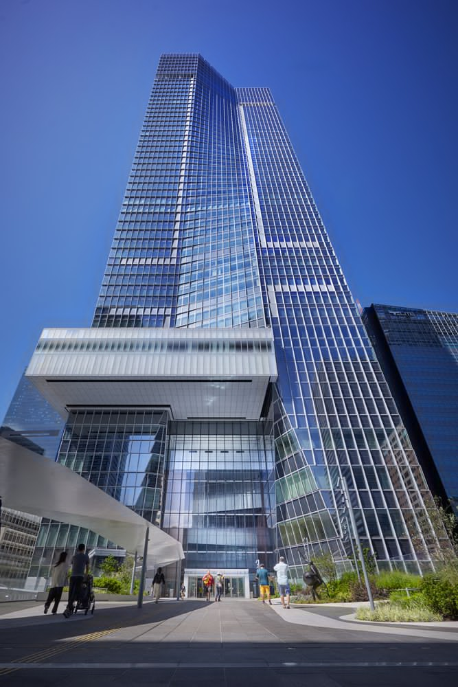 Ground-level view of the glass facade and podium entrance with pedestrians approaching