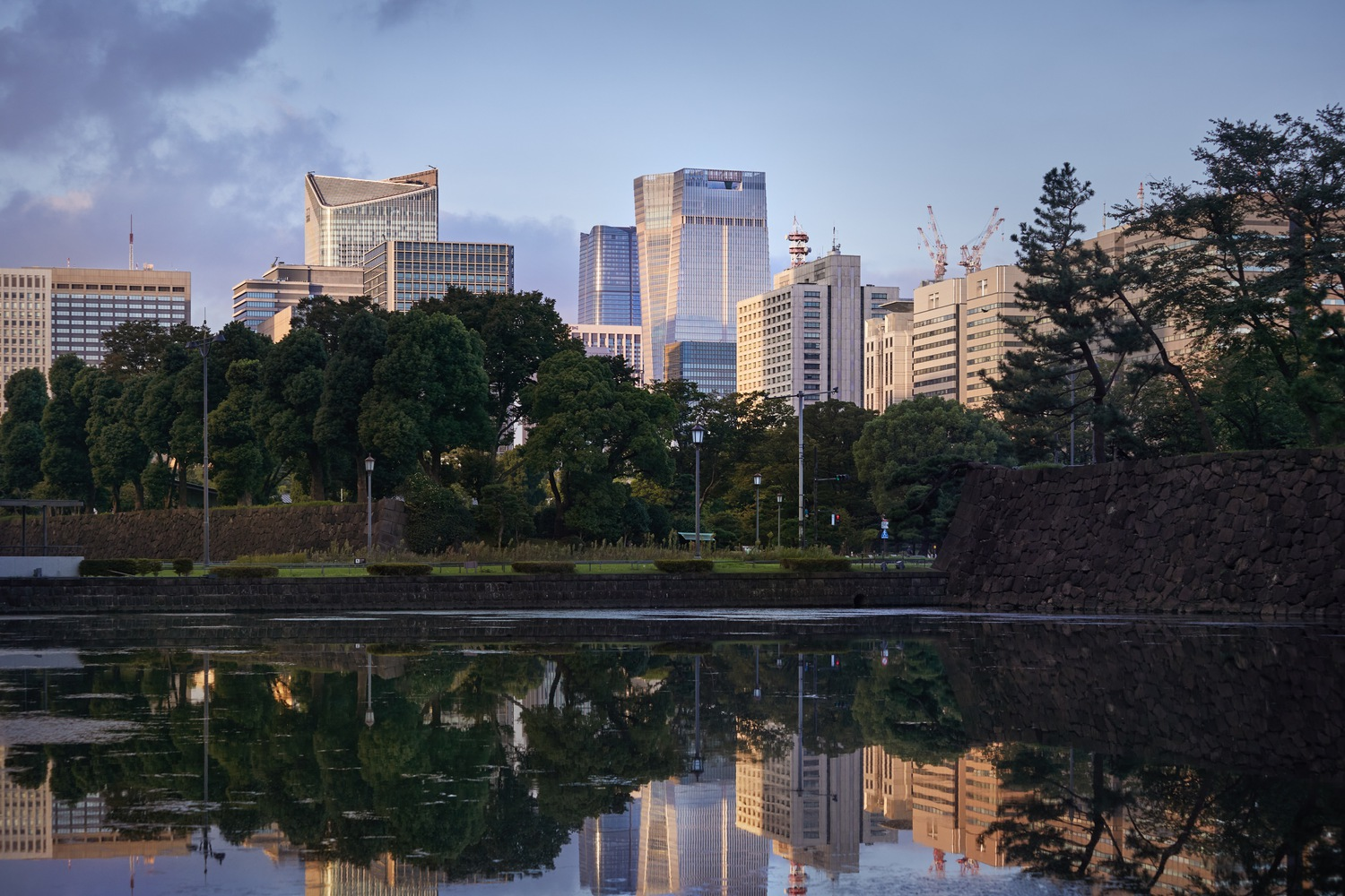 Tower reflected in moat water with stone embankment and trees at twilight