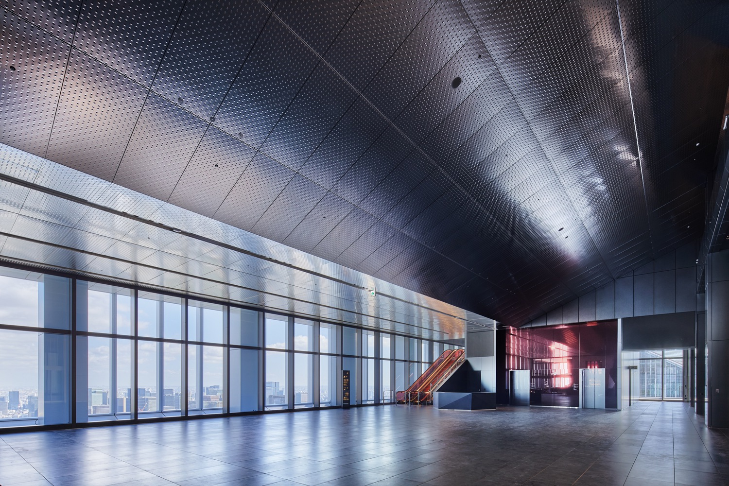 Interior lobby with floor-to-ceiling glazing, perforated metal ceiling, and distant escalator