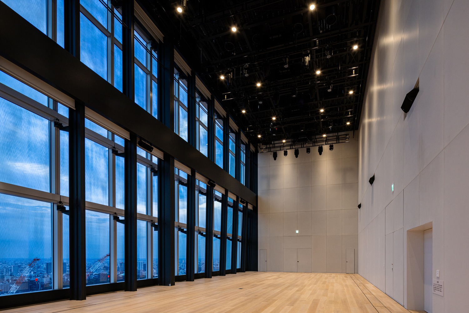 Performance hall with timber flooring, black ceiling grid, and gridded windows at dusk