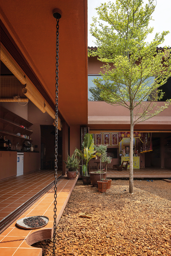 Central courtyard with gravel ground, young tree, and terracotta-tiled covered walkway under morning sunlight