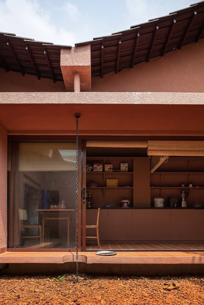 Covered porch with exposed timber rafters, sliding screen, and chain rain drain overlooking gravel courtyard