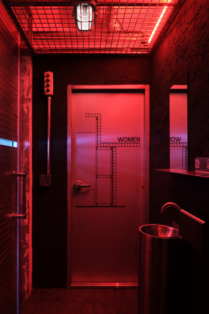 Restroom entrance illuminated by red LED lighting beneath a gridded ceiling panel