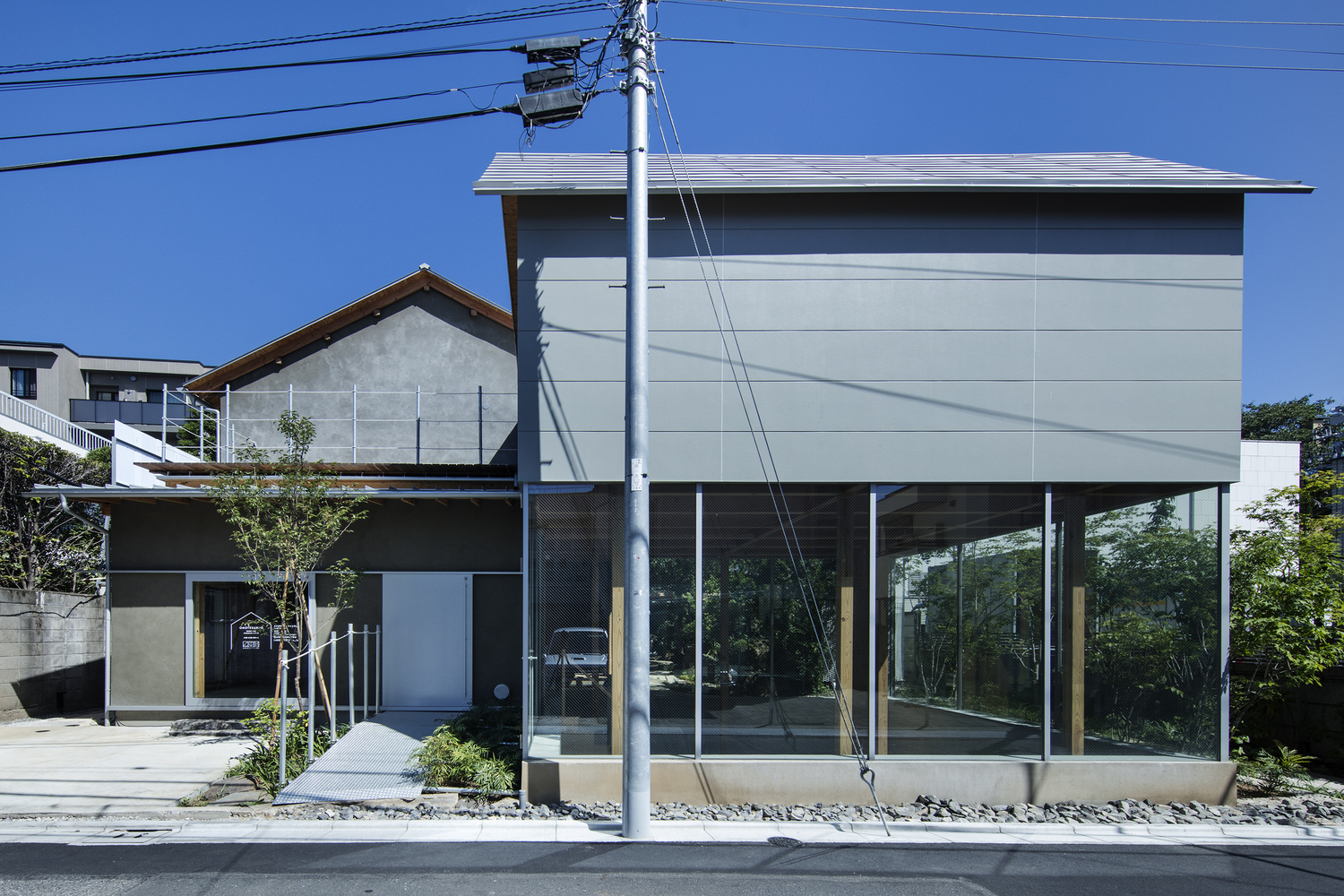 Two-story facade showing upper panel volume elevated above glazed ground floor beneath overhead power lines