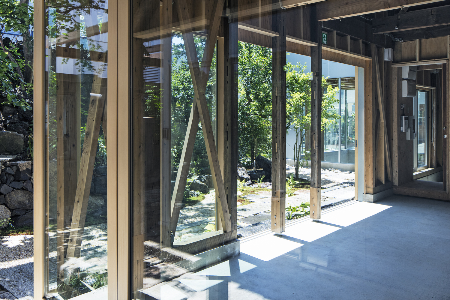 Glass walls with exposed timber framing opening onto a gravel courtyard with stepping stones
