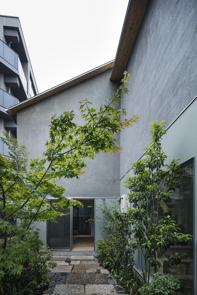 Smooth plaster facade with entrance door framed by young trees in a gravel courtyard