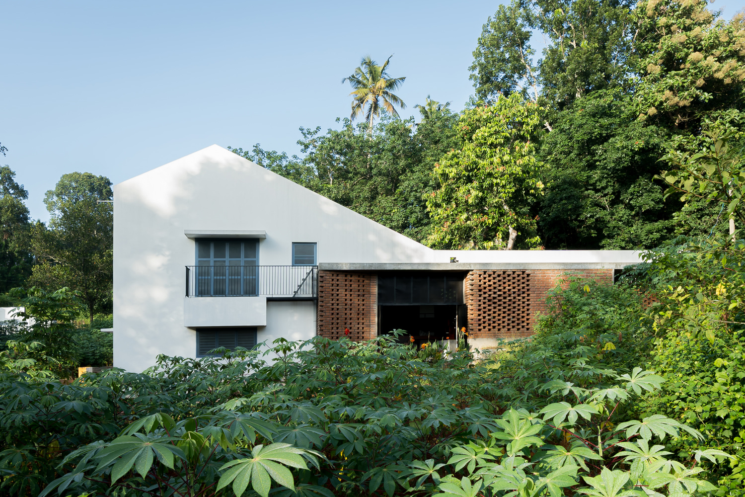 White gabled volume and brick pavilion with perforated screens surrounded by lush tropical vegetation