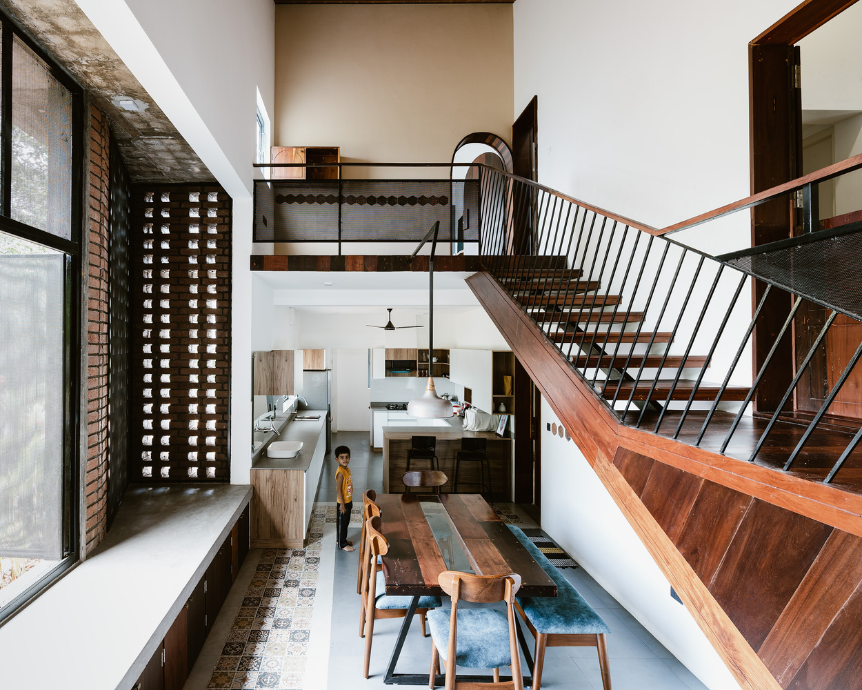 Double-height dining space with open timber staircase and perforated brick screen illuminated by skylight