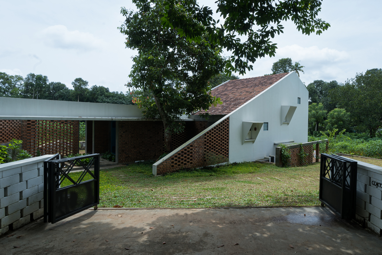 Entry courtyard view showing white gabled form and brick volumes with lattice screens under overcast sky