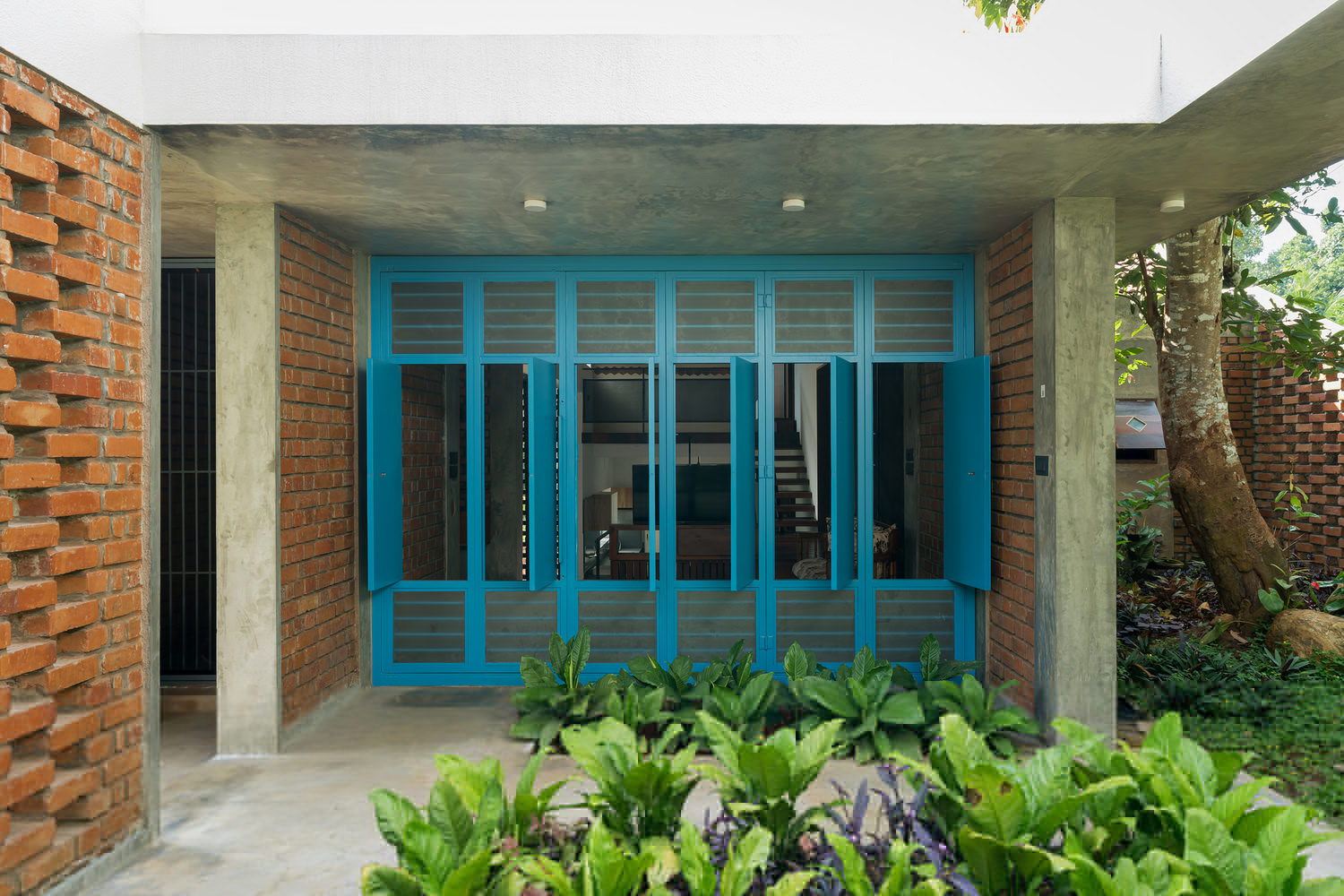 Covered courtyard with turquoise timber doors flanked by perforated brick walls and planted beds