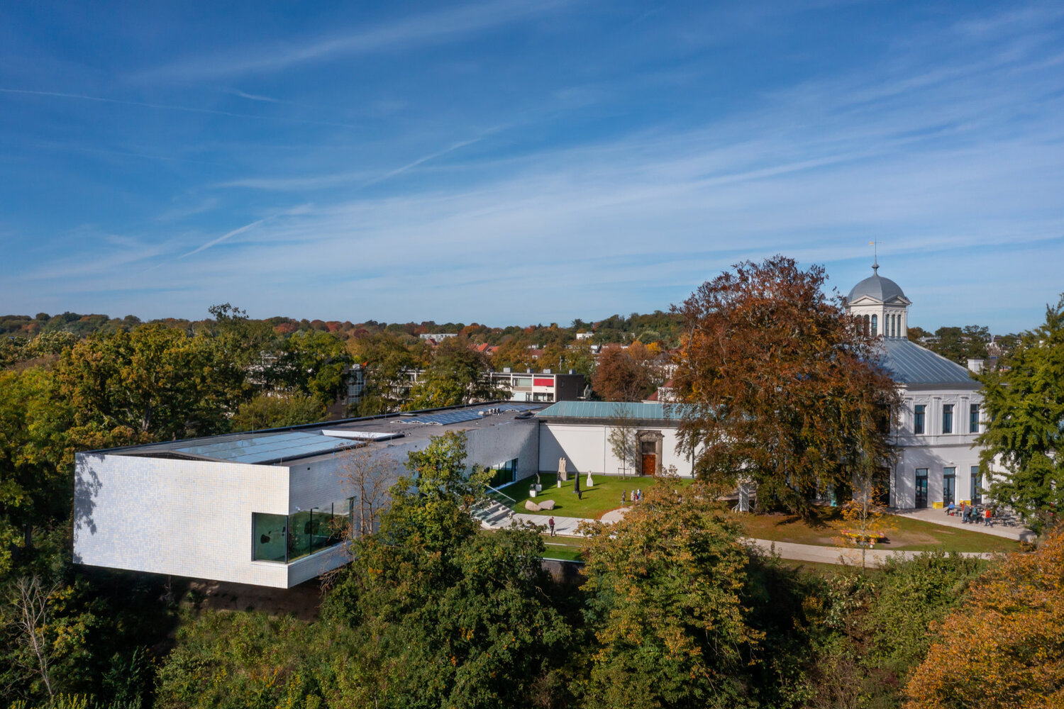 Aerial view of the white rectangular volume adjacent to a domed structure among autumn trees