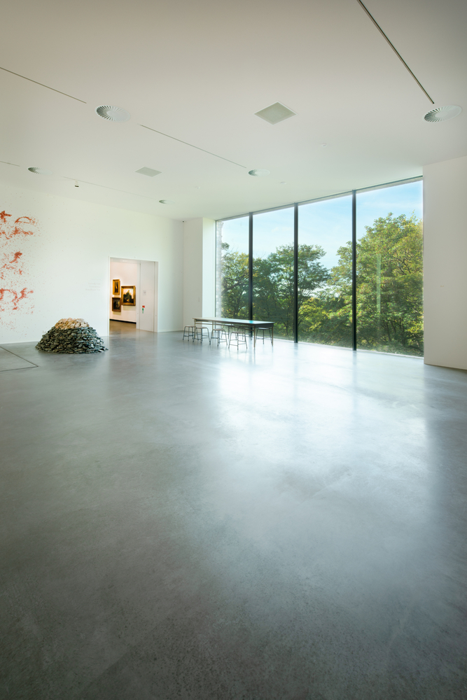 White-walled gallery space with polished concrete floor overlooking trees through full-height glazing