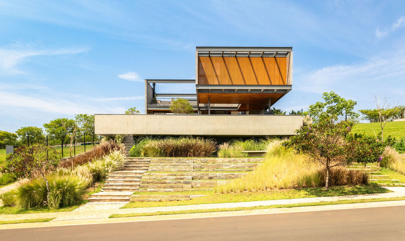 Street view of the cantilevered concrete base and timber-clad upper volume above a terraced hillside