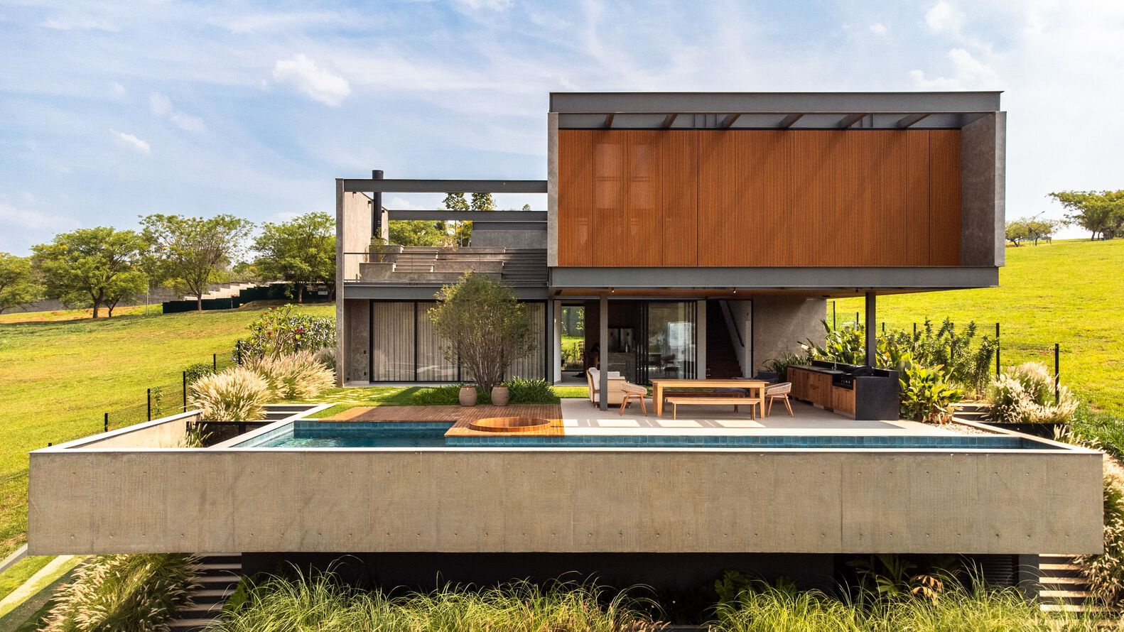 Rear elevation showing the concrete terrace with pool and timber screens against green rolling hills