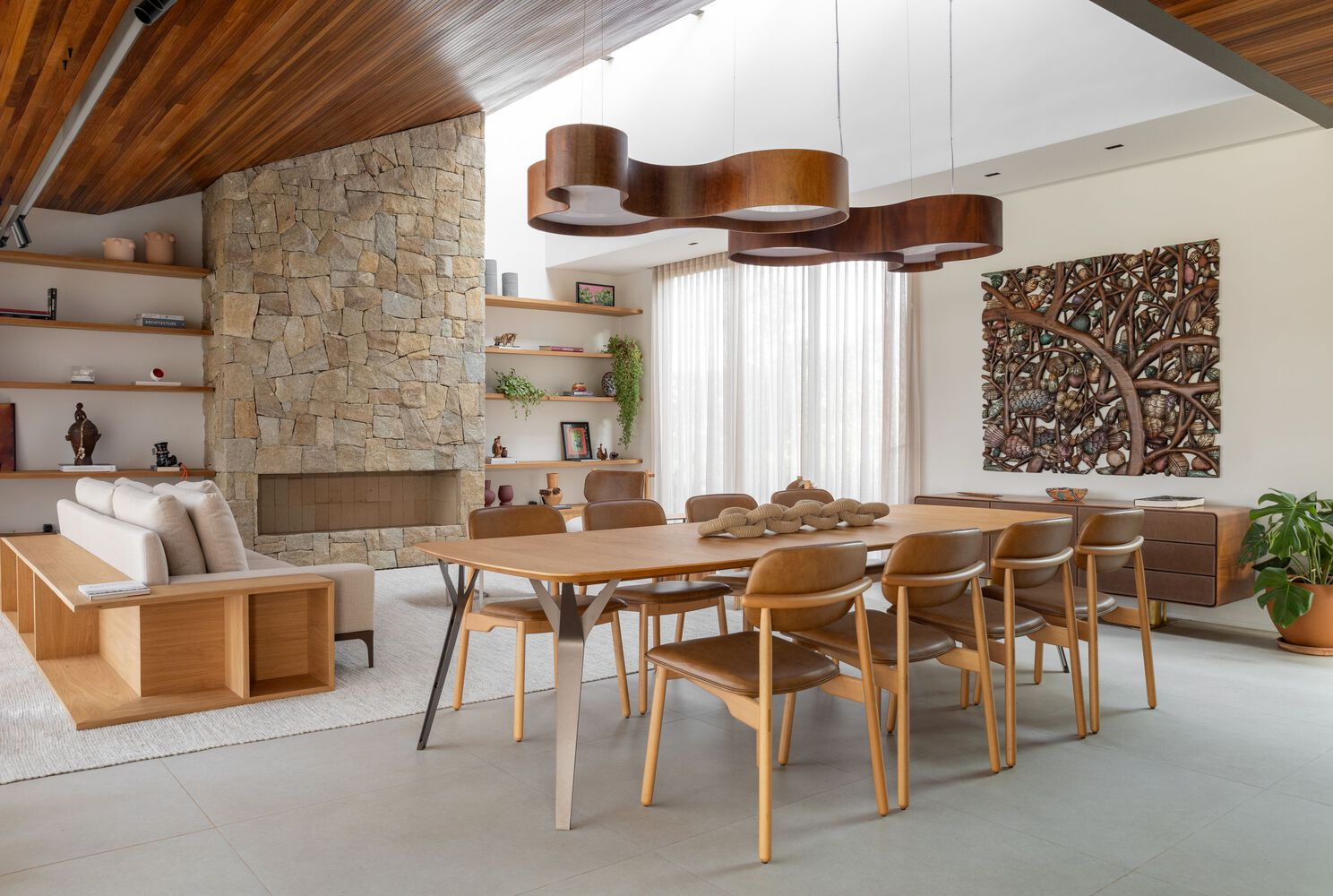 Open-plan dining area with wood-slat ceiling, stone fireplace wall and suspended timber light fixture