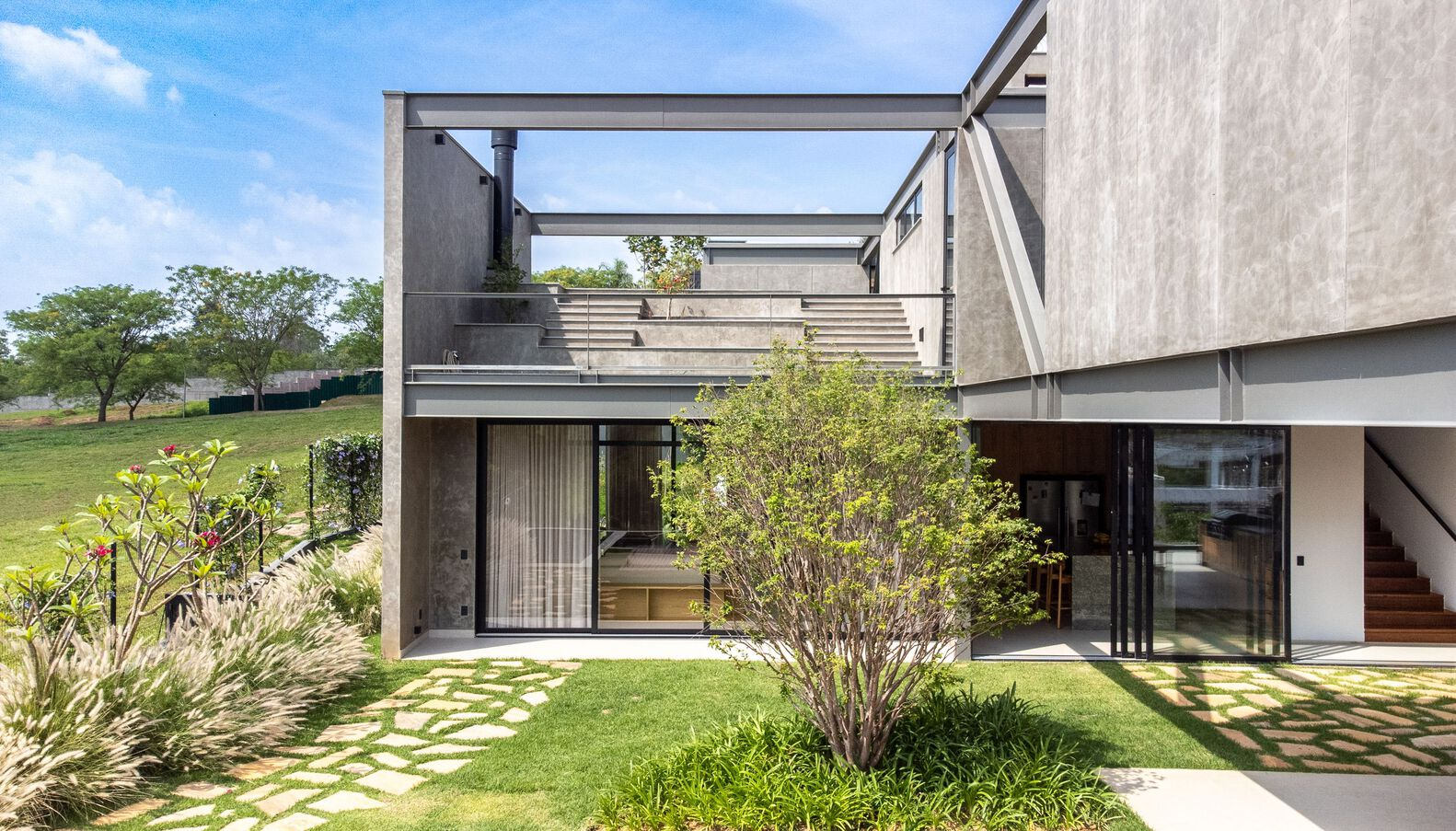 Garden courtyard with pavers and grasses between the glazed volumes and concrete frame above