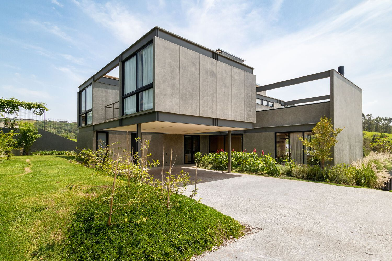Front entrance view showing concrete panel facade with steel frame pergola and planted driveway