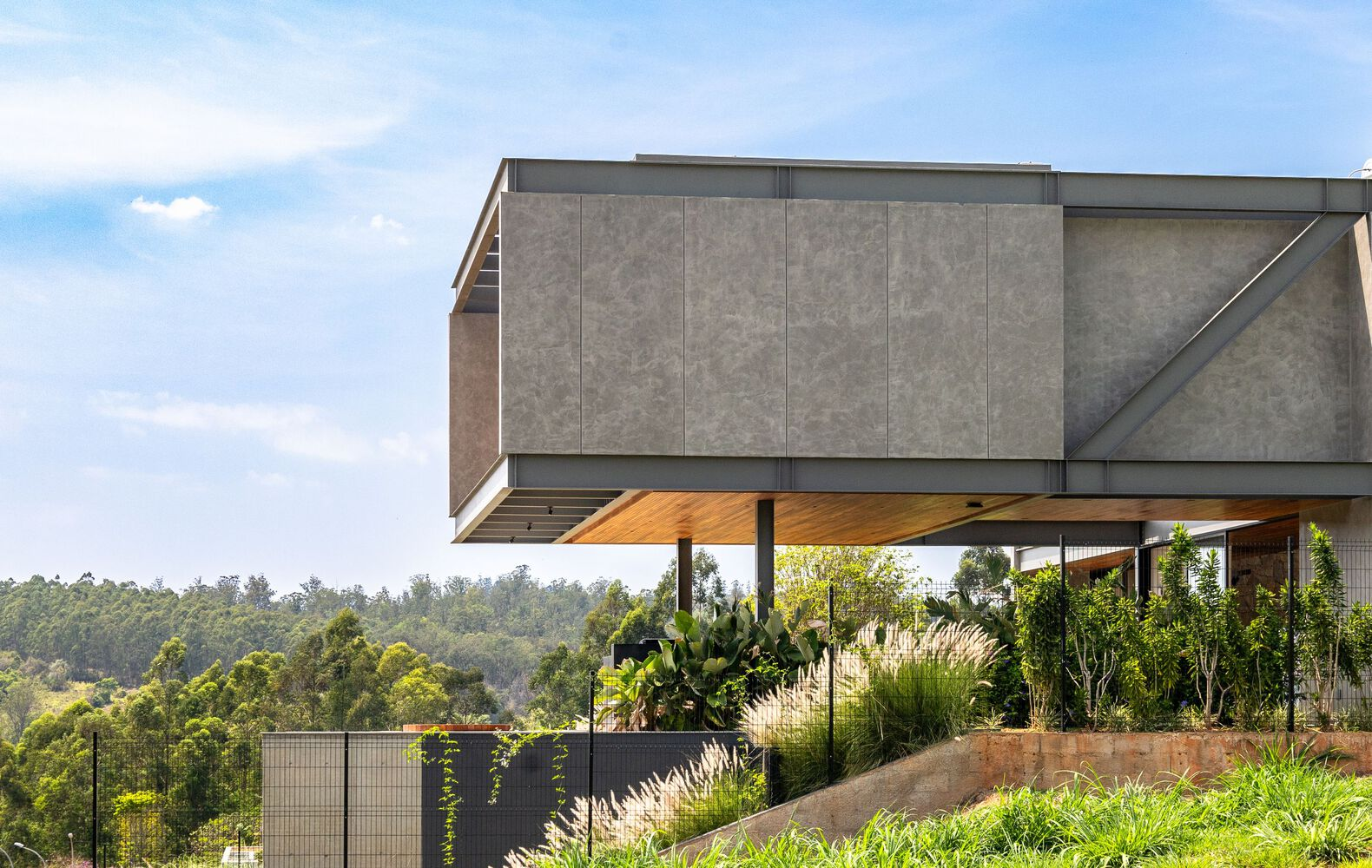 Cantilevered concrete volume suspended above terrace with planted beds overlooking forested hillside