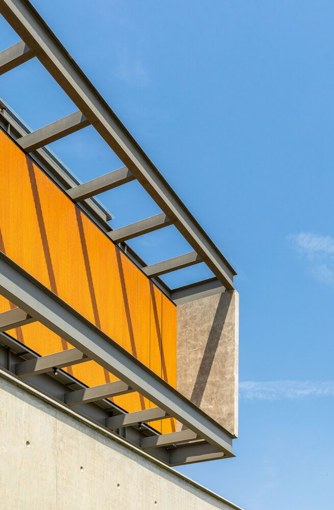 Upward view of steel brise-soleil shading amber glass panels on upper facade under clear sky