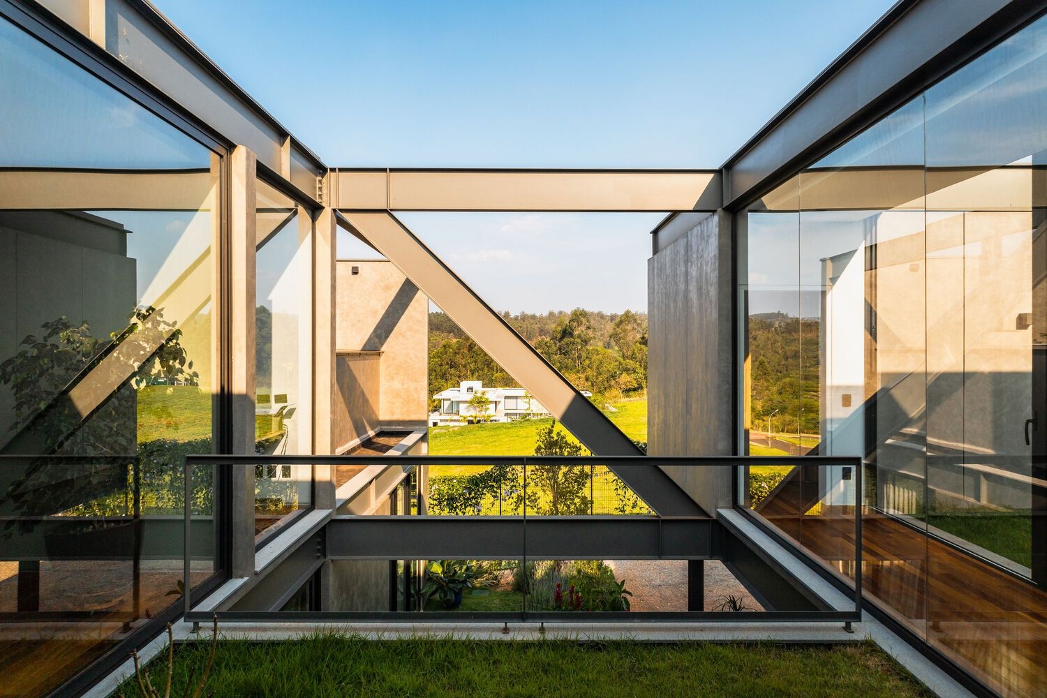 Glass-enclosed courtyard with steel cross-bracing framing views of distant landscape at dusk