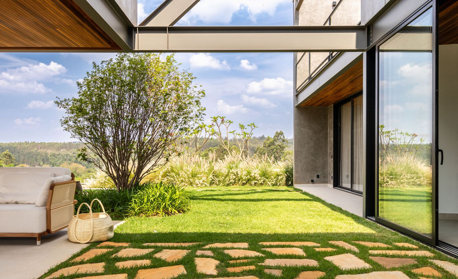 View from covered terrace through steel frame to stone-paved path crossing lawn with tree and distant hills