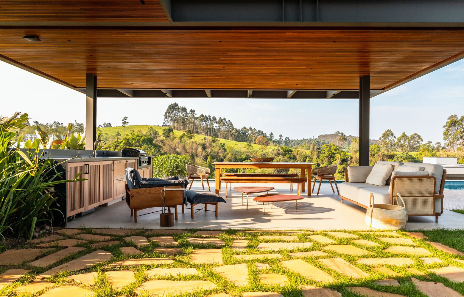 Covered outdoor terrace with timber ceiling and stone paving grid set in grass overlooking rolling landscape