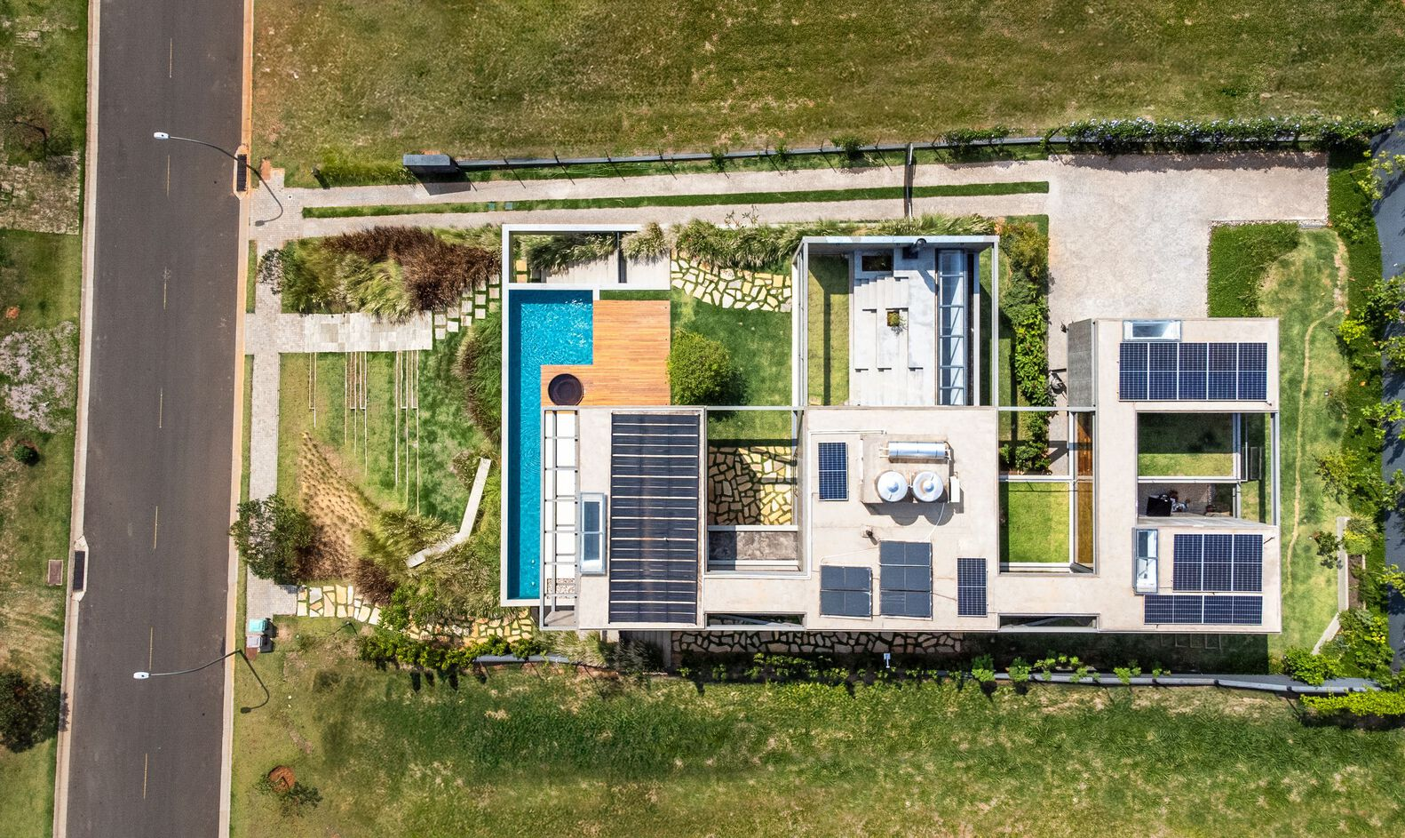 Aerial view of flat roof with solar panels, lap pool, and lawn patches beside residential street