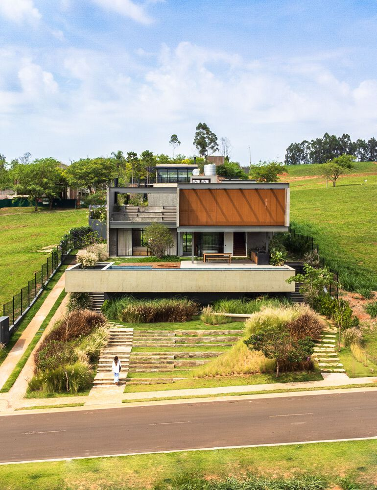 Street view of the terraced house with concrete and timber volumes set into a landscaped hillside