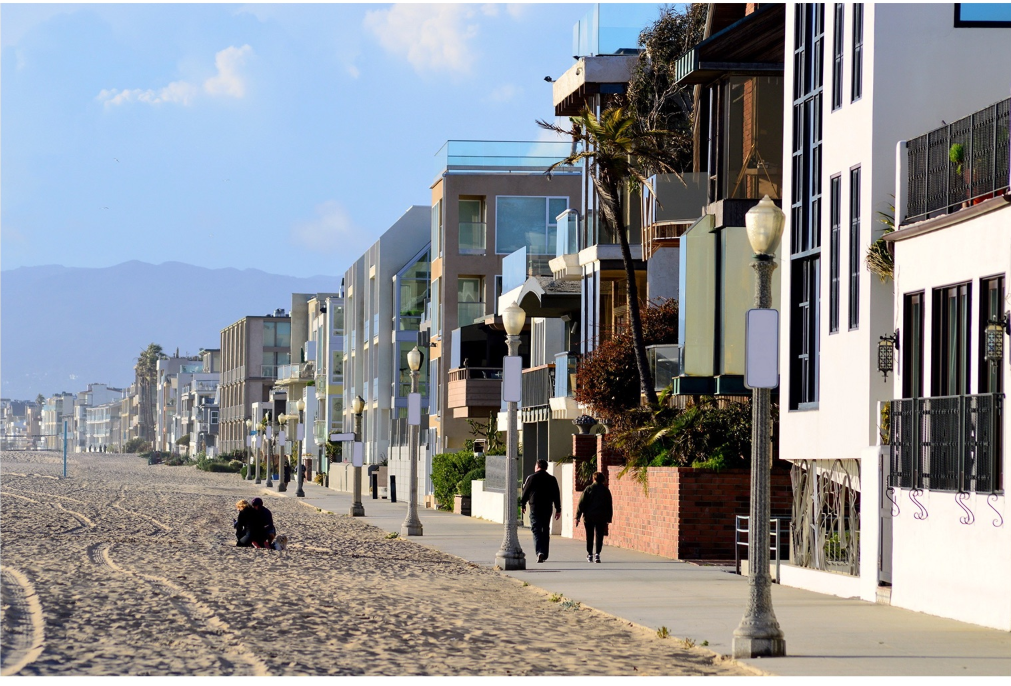 Beachfront boardwalk with mixed residential buildings and two pedestrians walking at sunset