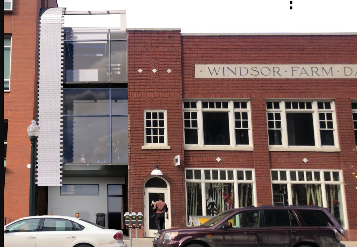 Historic brick building with white-trimmed windows next to a white tile facade with parked cars