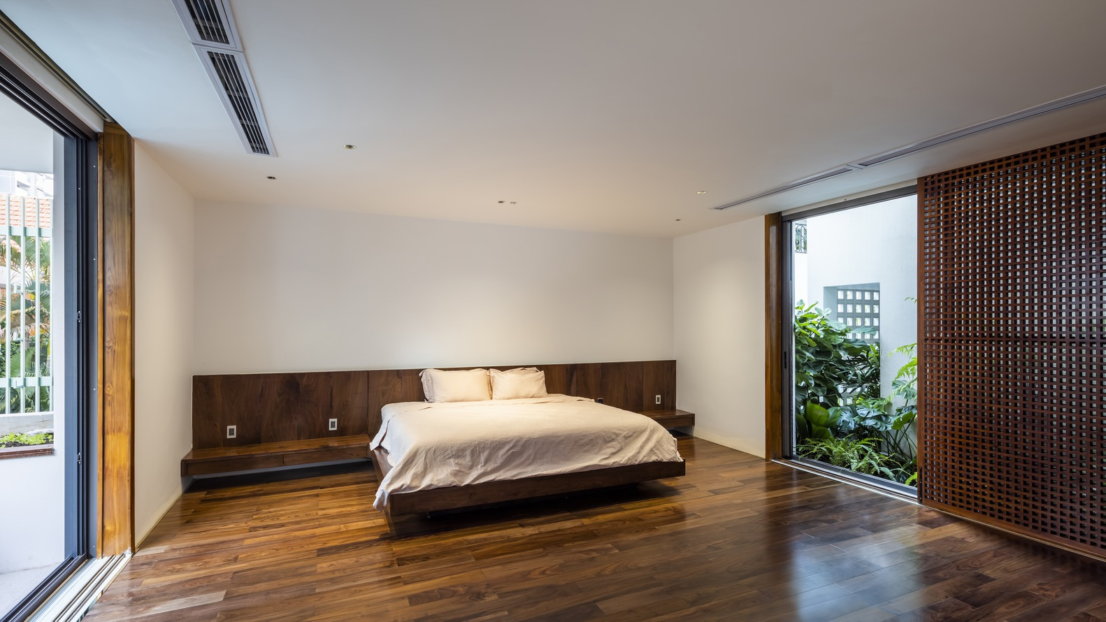 Bedroom with walnut platform bed and integrated headboard opening onto a planted terrace through sliding glass doors