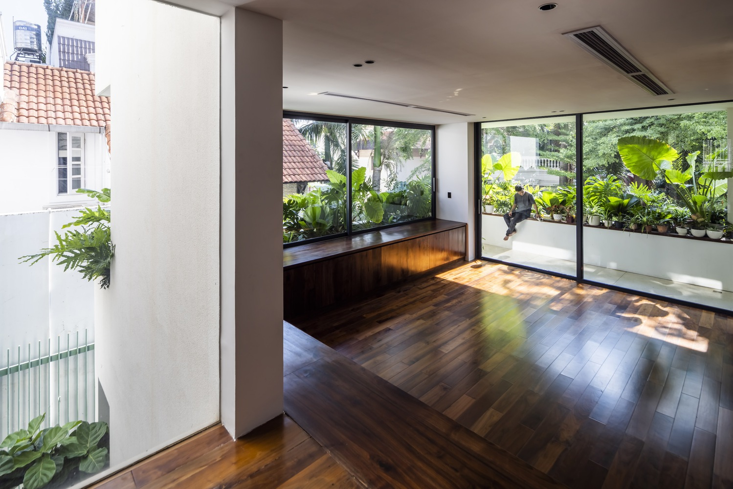 Interior room with walnut flooring and built-in cabinetry overlooking a green terrace with banana plants
