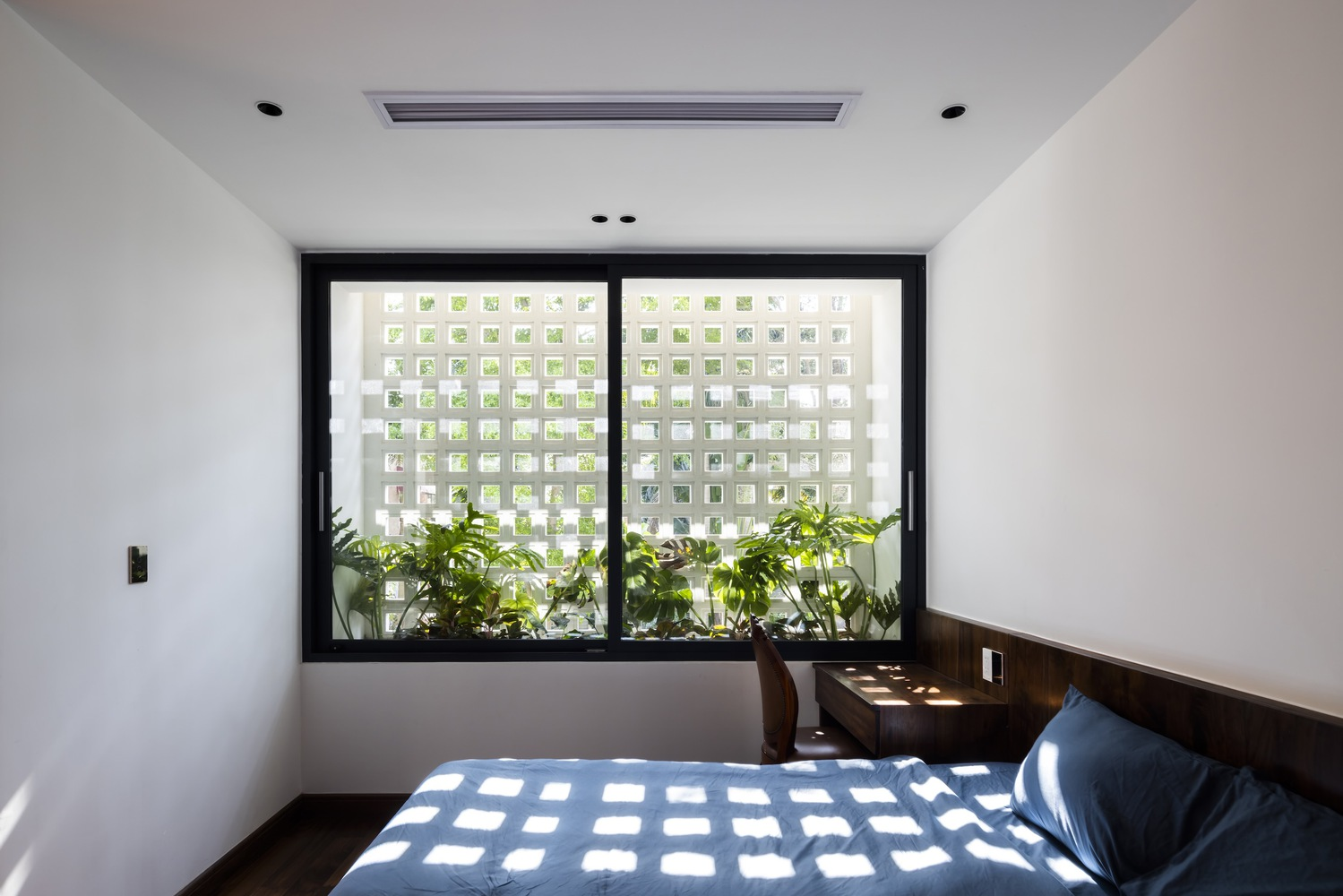 Bedroom window with perforated white screen filtering dappled sunlight onto potted plants on the sill