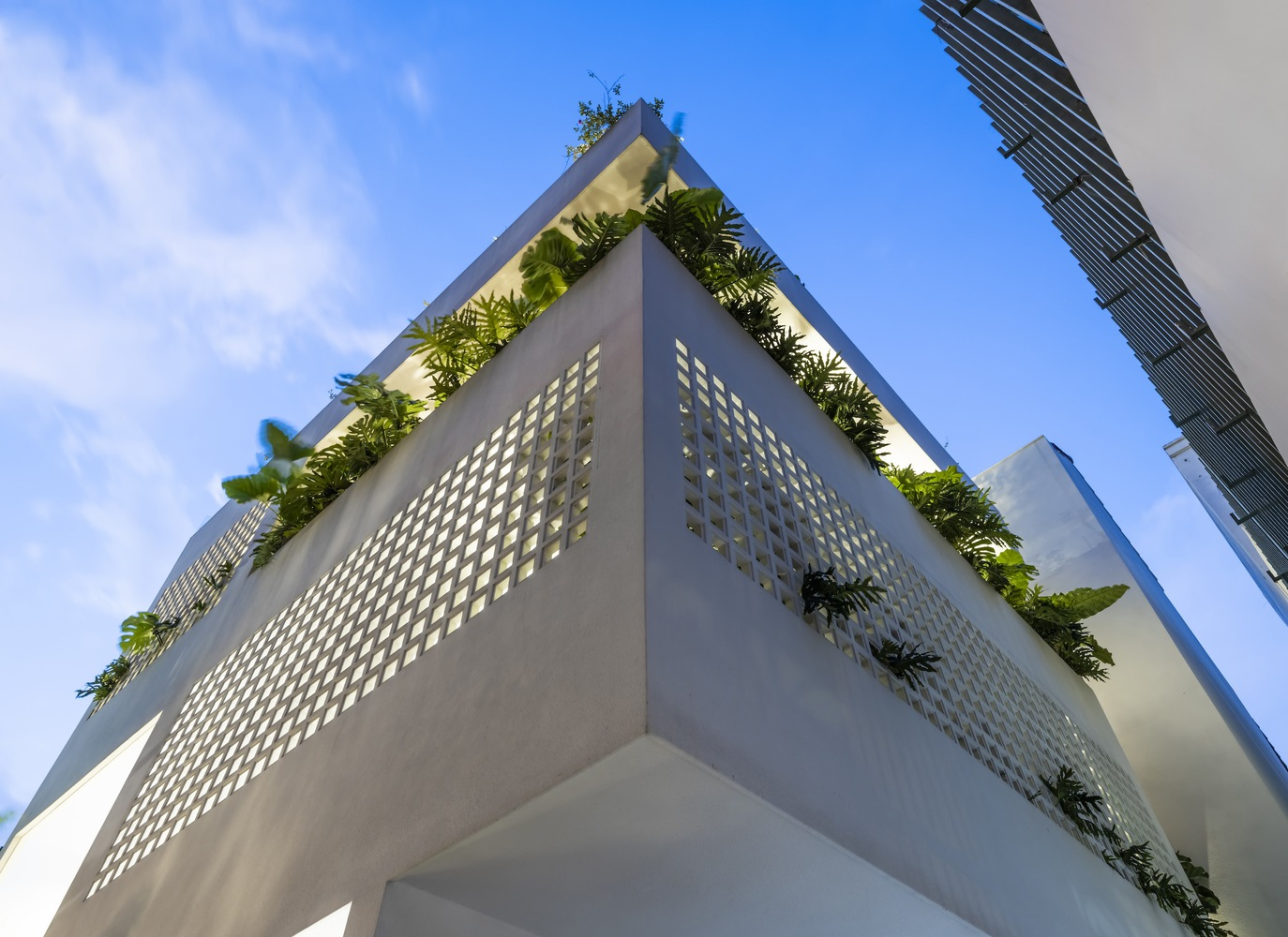Corner facade with perforated concrete panels and rooftop planted terraces under a clear blue sky