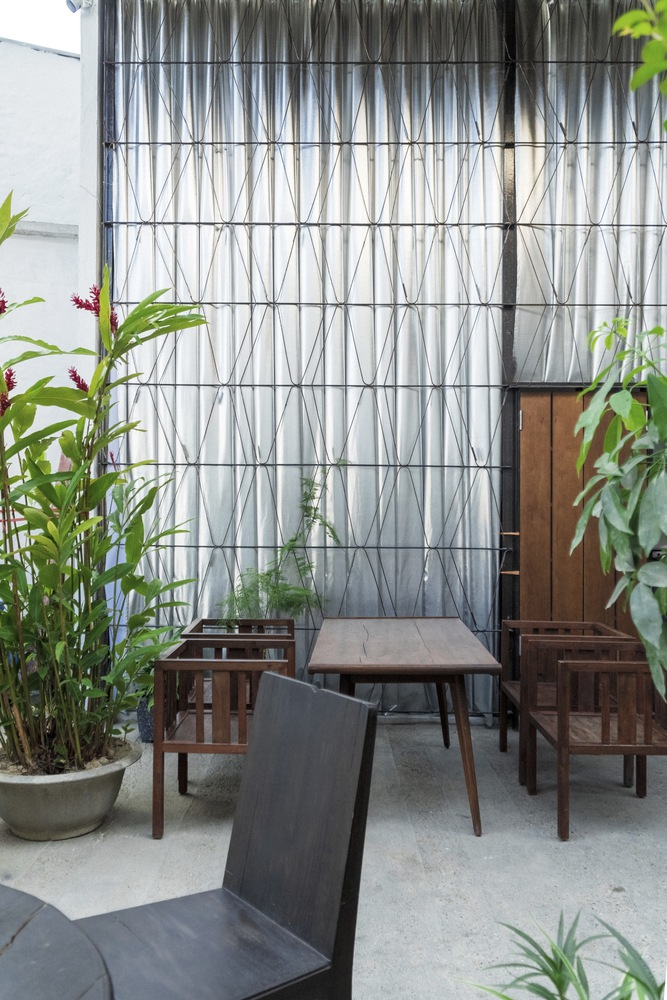 Wire trellis facade with bamboo planting and timber furniture on a concrete floor