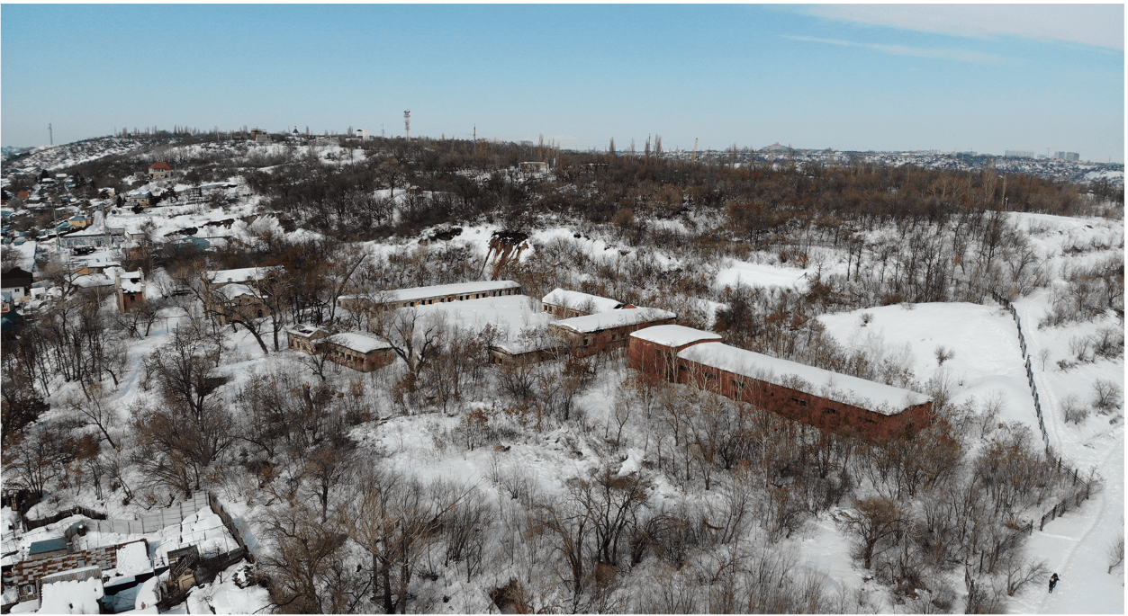Aerial view of three linked brick pavilions nestled among bare trees in a snowy hillside landscape