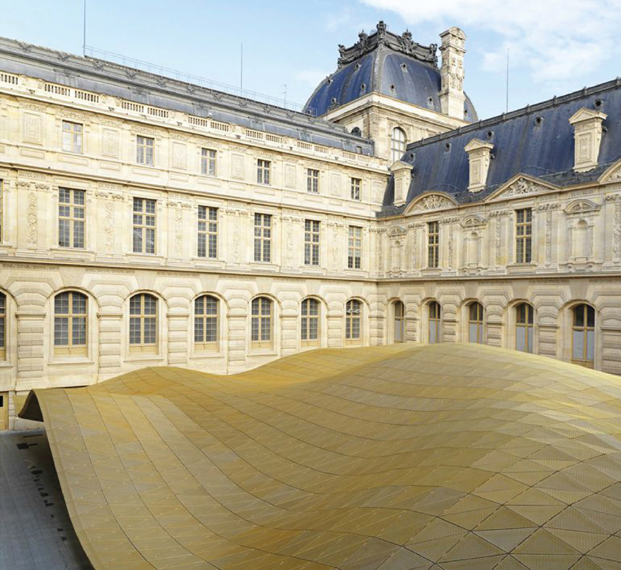 Courtyard with sloping timber deck surface enclosed by pale stone arcaded facades and a mansard roof