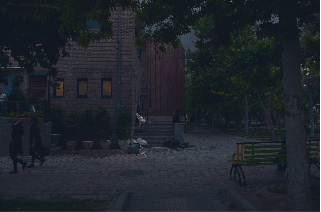 Brick building with corrugated metal extension and entrance steps visible through trees at dusk
