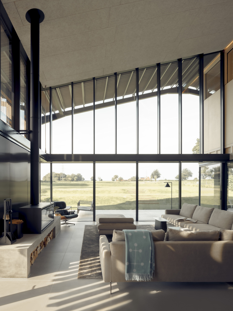 Double-height living space with floor-to-ceiling glass wall and freestanding black stove under concrete ceiling beams