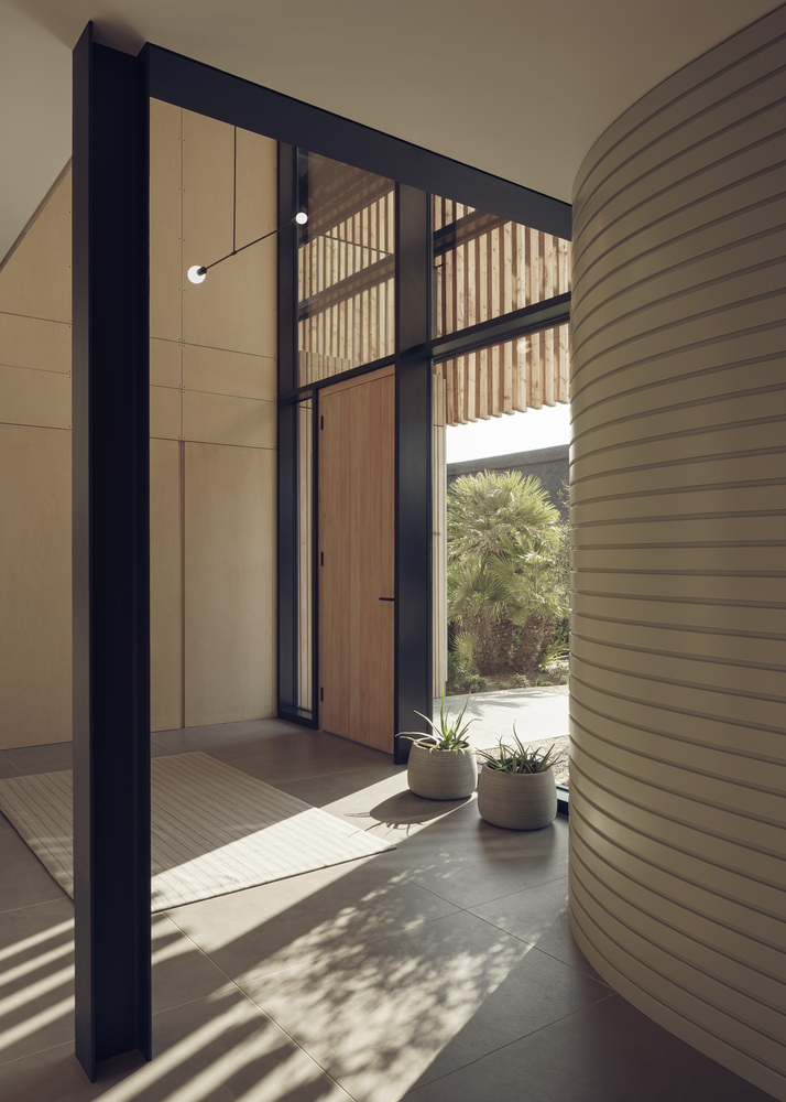 Entry vestibule with timber door framed by black steel and vertical slat screen in afternoon light